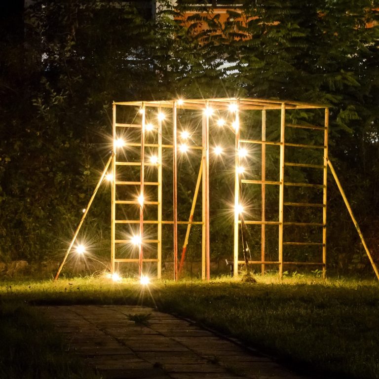 Ein beleuchtetes, ostdeutsches Klettergerüst im Freien umgeben von Gras und Bäumen bei Nacht.