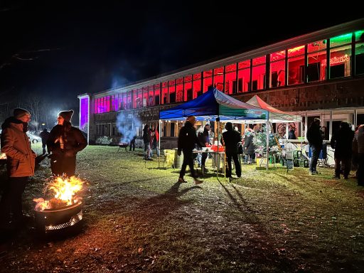 Nachtliche Feier mit bunten Lichtern, Zelten und Menschen am Lagerfeuer.